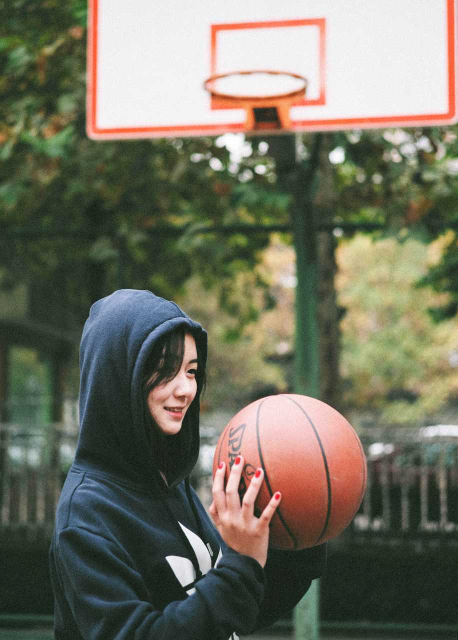篮球女孩坐在球场中央的篮球上休息，目光温柔地抚摸着球面，像在与老朋友分享心事